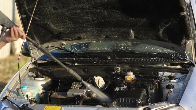 Young attractive man perfusing with water his silver car