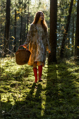 Young woman with long red hair in a linen dress gathering mushrooms in the forest in the bast basket