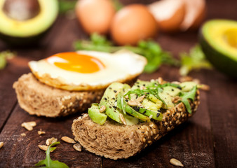 Two different bruschettas with avocado, rucola sesame, seeds, egg on wooden table