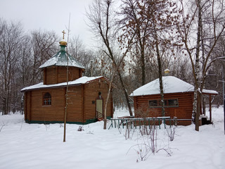 Christian log church in the snow. Winter season. Kyiv, Ukraine. Golden domes. Church in the forest or park