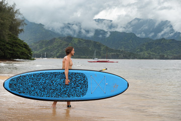 Stand up paddleboard fit man carrying paddle board going on ocean swim watersport activity at Puu...