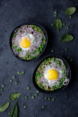 Bowls with green pea soup, fried egg and spinach leaves on black background, top view.