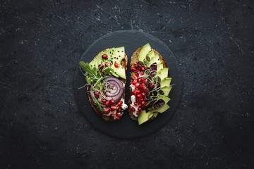 Healthy food. Avocado toasts with avocado slices, seeds and sprouts on dark background.