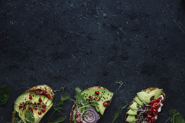 Top view of avocado toasts with seeds and sprouts on dark background with copy space.