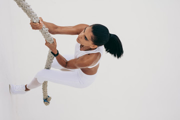 Fitness woman climbing a wall using a rope