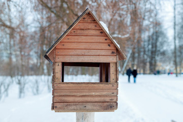 Obraz na płótnie Canvas Winter landscape. Wooden birdhouse in snow-covered park. In the distance a couple walking down the path. Blurry photography with a shallow depth of field. Cold winter day.