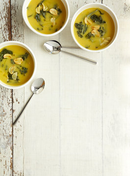 3 Bowls of Butternut Squash, kale soup with garlic on White Wood surface