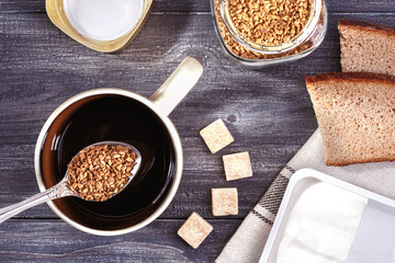 Black coffee and bread,butter, cheese in box on grey wooden table. Top view.