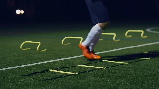 Soccer agility training equipment. Professional football player with agility ladder and hurdles at night, 4k slow motion