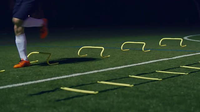 Soccer agility training equipment. Professional football player with agility ladder and hurdles at night, 4k slow motion