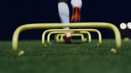 Soccer agility training equipment. Professional football player with training hurdles at night. 4k slow motion