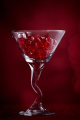 Martini glass filled with red valentine crystal hearts surrounded by bokeh on a red background