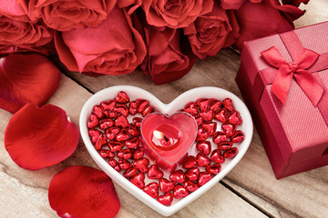 Festive background to the Valentine's day. A bouquet of red roses, a gift box, a heart-shaped plate and a heart-shaped candle. On a wooden background.
