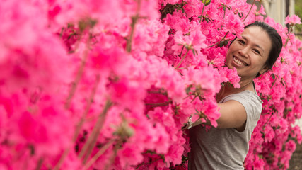 Asian woman standing in front of pink azalea flowers in tshirt on hot spring day