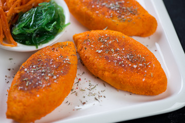 Closeup of roasted cutlets made of carrot and served on a white plate, horizontal shot