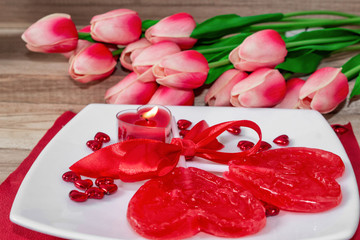 Lollipops in the form of a heart on a plate with candles and tulips flowers. Festive background to the Valentine's day.
