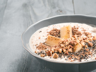 Close up view of overnight oats in bowl with banana, LSA, chia seeds, almond and honey on gray wooden table background. Healthy breakfast oatmeal recipe idea
