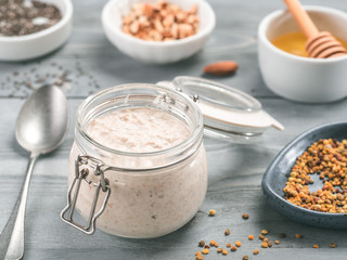 Overnight oats in jar and ingredients - chia seeds, almond, honey and pollen on gray wooden table background. Healthy breakfast oatmeal recipe idea