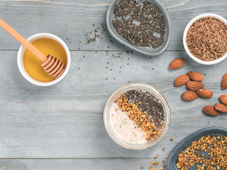 Overnight oats in jar and ingredients - chia seeds, almond, LSA, honey and pollen on gray wooden table background. Healthy breakfast oatmeal recipe idea. Top view