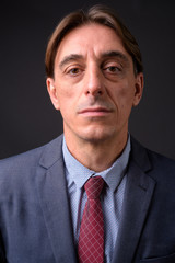 Mature handsome Italian businessman against gray background