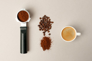 Cup of black coffee next to coffee beans and grains, handle coffee machine filter on gray background, minimal concept, closeup, Morning coffee routine