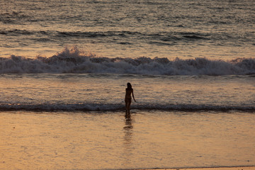 Fototapeta na wymiar girl on the background of high waves of the ocean at sunset