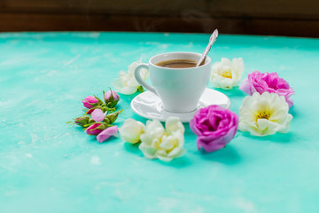 Fototapeta na wymiar colorful flowers and morning Cup of coffee on blue background. the concept of hot drink, coffee for Breakfast. minimal flat lay.Romantic table with hot drink cup and roses.beautiful flowers for