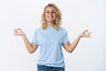 Fototapeta premium Keep calm and carry on. Portrait of optimistic relieved and stress-free good-looking female with blond hair smiling pleased and relaxed, standing in meditating pose in nirvana, showing orbs