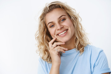 Close-up shot of sincere happy and charismatic attractive european blonde with blue eyes in t-shirt smiling carefree and happy holding fingers on cheek cute and flirty, gazing kind at camera