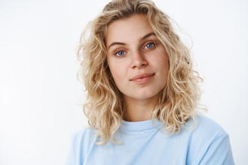 Naklejka premium Charming and cute sincere blonde woman with short curly hairstyle and blue eyes in t-shirt tilting head intrigued smiling flirty and gazing at camera with interest over white background