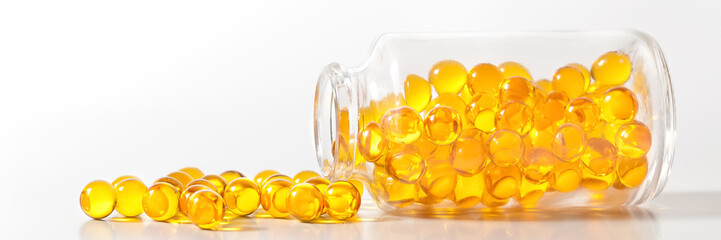 Yellow pill capsules crumble from a glass bottle on a white background.