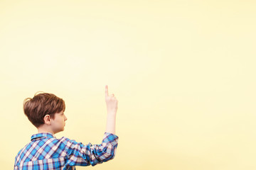 look there. approval. cute boy pointing upwards with index finger over yellow background, advertisement, banner or poster template, emotion facial expression, people reaction