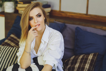 Young beautiful blonde girl in a white men's shirt on the bed