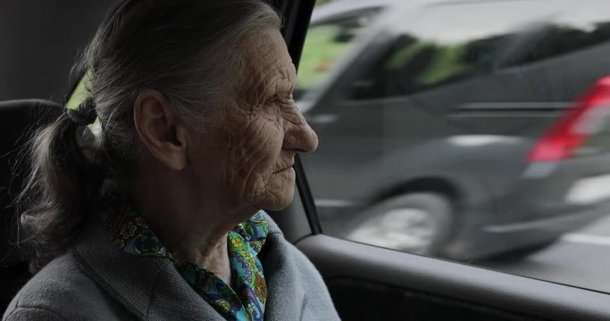 A grandmother with deep wrinkles sits in the car and looks out the window.