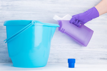 hand in a purple rubber glove pours detergent into a blue bucket
