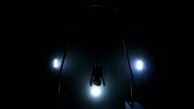 Gymnast on a dark background stands on his hands using rings in the air. Performs rotation in the Olympic program in slow motion 120 fps. gymnastic rings, professional gymnast