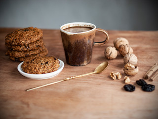 oatmeal cookies, brown mug with cocoa, walnuts, cinnamon, prunes, vintage spoon on the wooden table