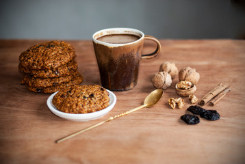 oatmeal cookies, brown mug with cocoa, walnuts, cinnamon, prunes, vintage spoon on the wooden table