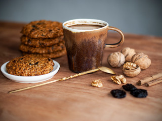 oatmeal cookies, brown mug with cocoa, walnuts, cinnamon, prunes, vintage spoon on the wooden table