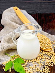 Milk soy in jug with spoon and leaf on dark board
