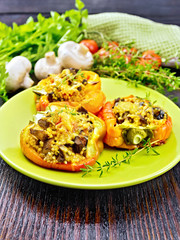 Pepper stuffed with mushrooms and couscous in green plate on wooden table