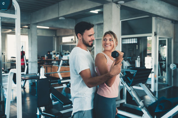 Sporty couple exercising dumbbell weights lifting in fitness gym., Portrait of attractive young couple are practicing workout in training class., Beautiful woman with trainer exercise weights lifting.
