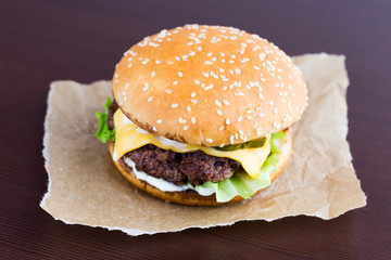 Burger on a table made of wood. Beef patty burger, cheddar cheese, lettuce, bacon, pickled cucumber, tomato and balsamic sauce.