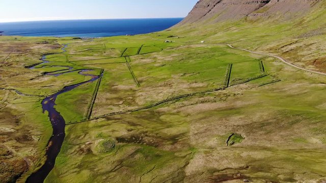 Rvier meandering to the sea through green fields, near Bolungarvik, Iceland