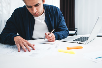 Concentrated building designer working with drawing plan and competer while sitting by the table at studio office. Young acrhitect using laptop and blueprint project