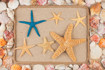 Frame made of rope, stars and seashells on the sand, with place for your image, text.