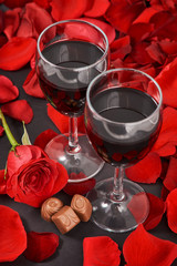 two glasses of wine, rose, petals and chocolates on a black background