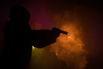 Silhouette of man with assault rifle ready to attack on dark toned foggy background or dangerous...