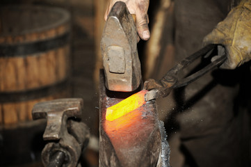 Blacksmith working metal with hammer on the anvil