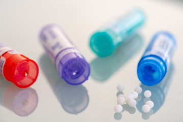 Homeopathic globules scattered around with their colored containers in the shape of tube